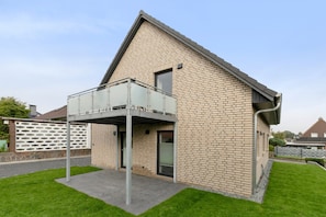 Ett modernt hus med en fasad av tegel, en balkong och en välskött gräsmatta.
