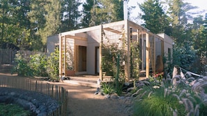 A wooden structure with an open design, surrounded by a garden with various plants and a wooden fence.