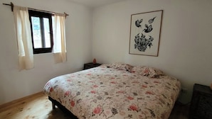 A bedroom with a bed, a window with curtains, a nightstand, and a wall-mounted artwork.