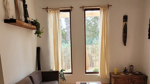 A living room with a sofa, a wooden coffee table, a colorful bench, a small table with a candle, and a window with curtains.