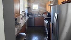 Cocina compacta con armarios de madera, refrigerador de acero inoxidable, lavavajillas y ventana que proporciona luz natural.