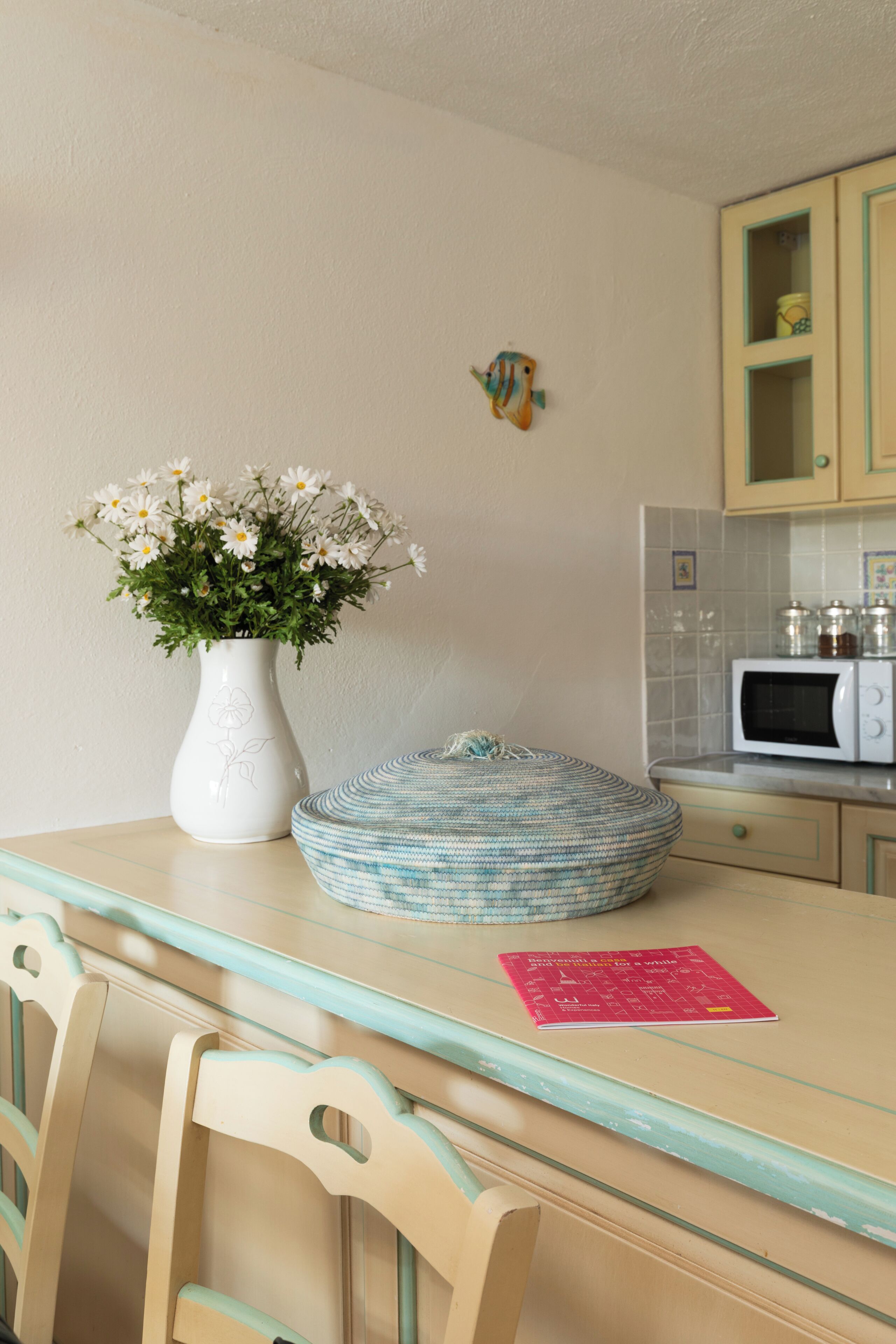 A kitchen with a white vase of flowers, a blue woven basket, and a microwave.