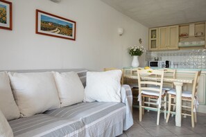 A cozy living room with a sofa, a dining table, and chairs. There is a kitchen area with cabinets and a microwave. - Alba Marina by Wonderful Italy (Olbia)