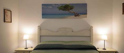 Un dormitorio con cama, dos mesitas de noche, una mesilla de noche, cabecero y un cuadro de un árbol en la pared.