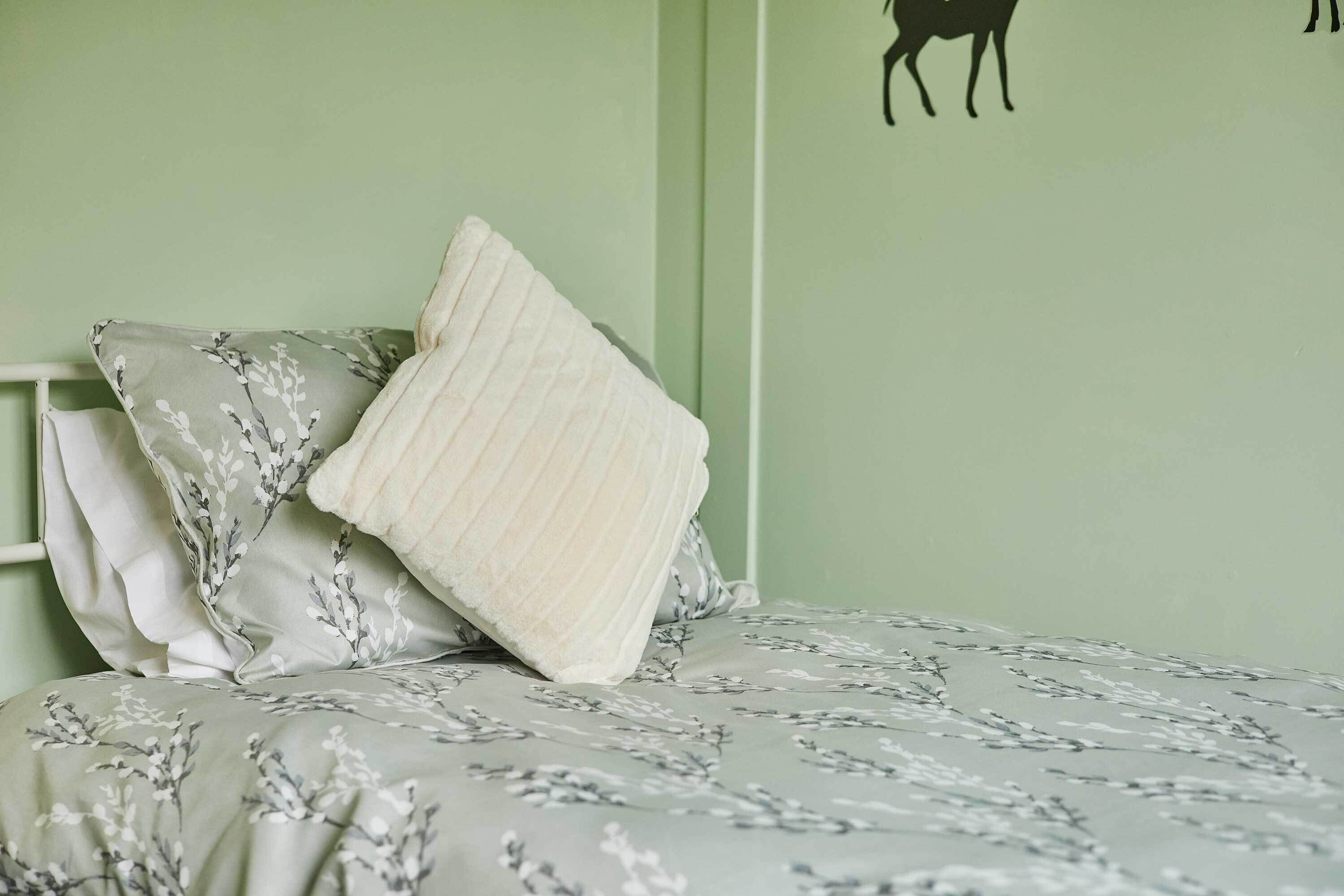 Een bed met bloemenbeddengoed, een kussen en een muur met een zwart silhouet.