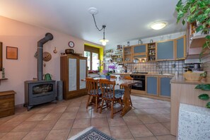 Una cocina con estufa, armarios de madera, una mesa de comedor con sillas y piso de baldosas.
