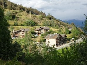 A hillside village with stone houses, a winding road, and a mountain backdrop.