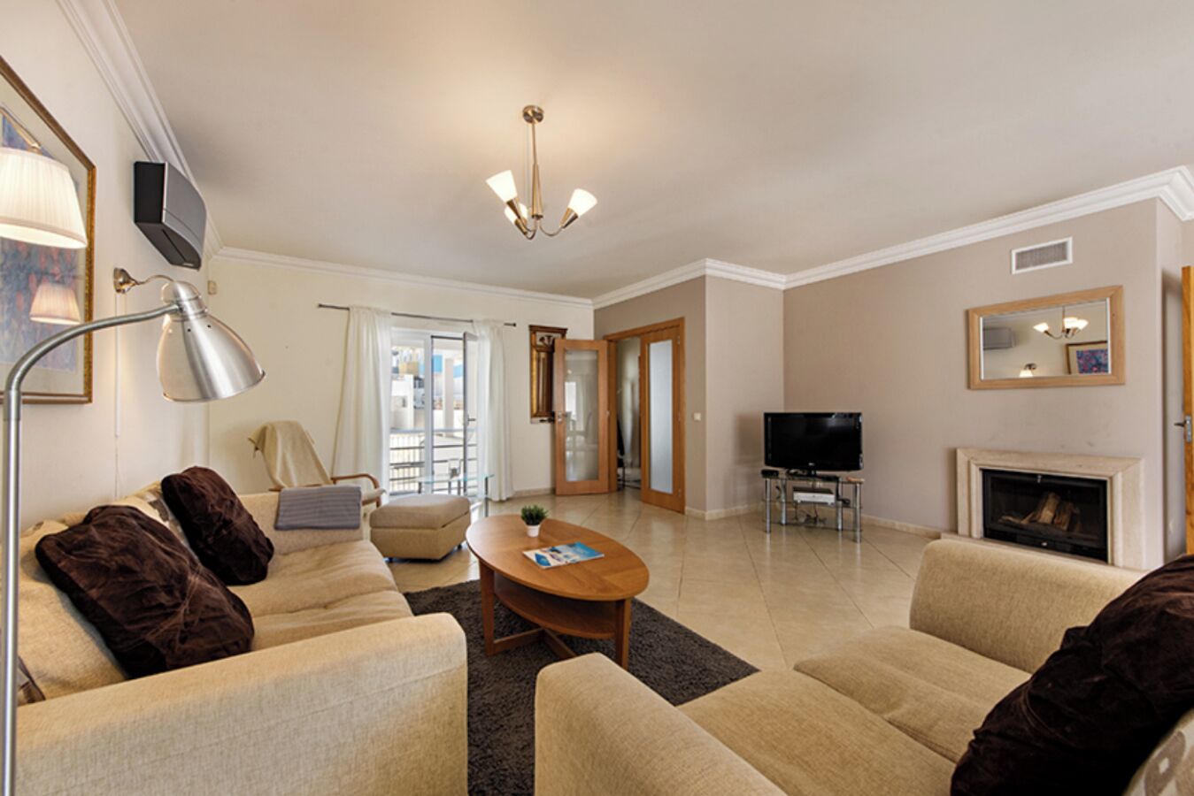 A living room with a sofa set, a coffee table, a TV, a fireplace, and a door leading to a balcony.