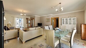 Uma sala de estar moderna com sofá, cadeiras, uma mesa de jantar de vidro e uma televisão.
