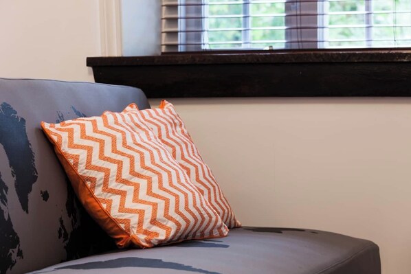 A sofa with a patterned cushion and a window with blinds.