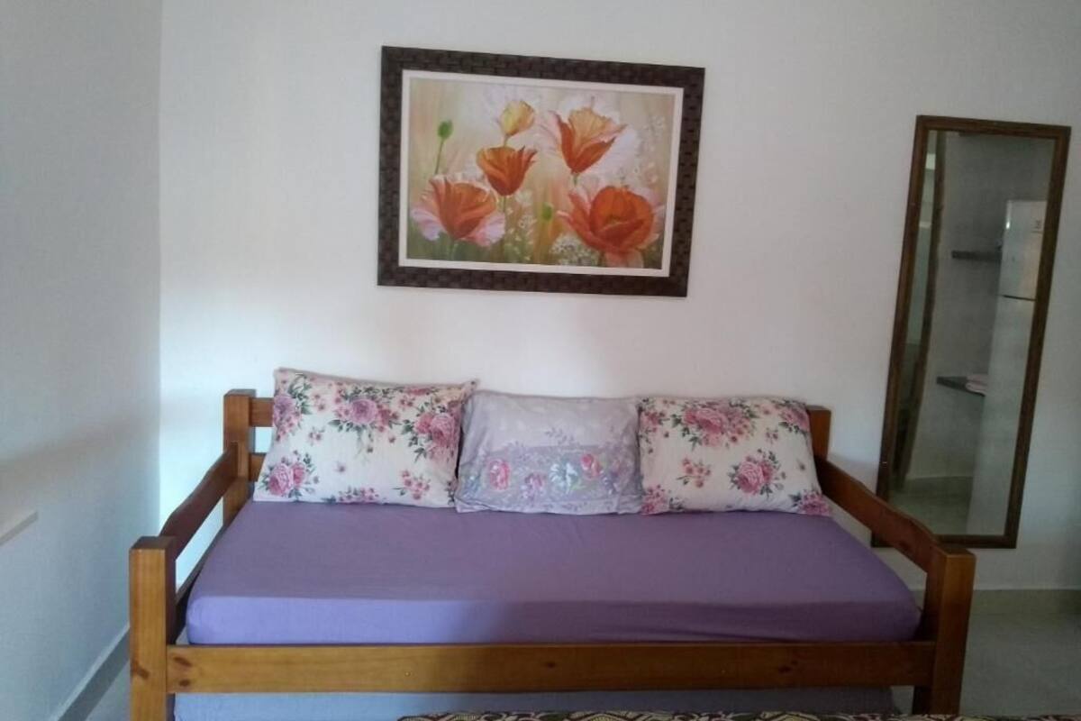 Una cama con almohadillas estampadas con flores, una colcha morada y un cuadro con motivos florales en la pared.