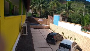 Ein Parkplatz mit zwei Autos, ein Gebäude mit gelber Fassade und Blick auf Palmen und Hügel.