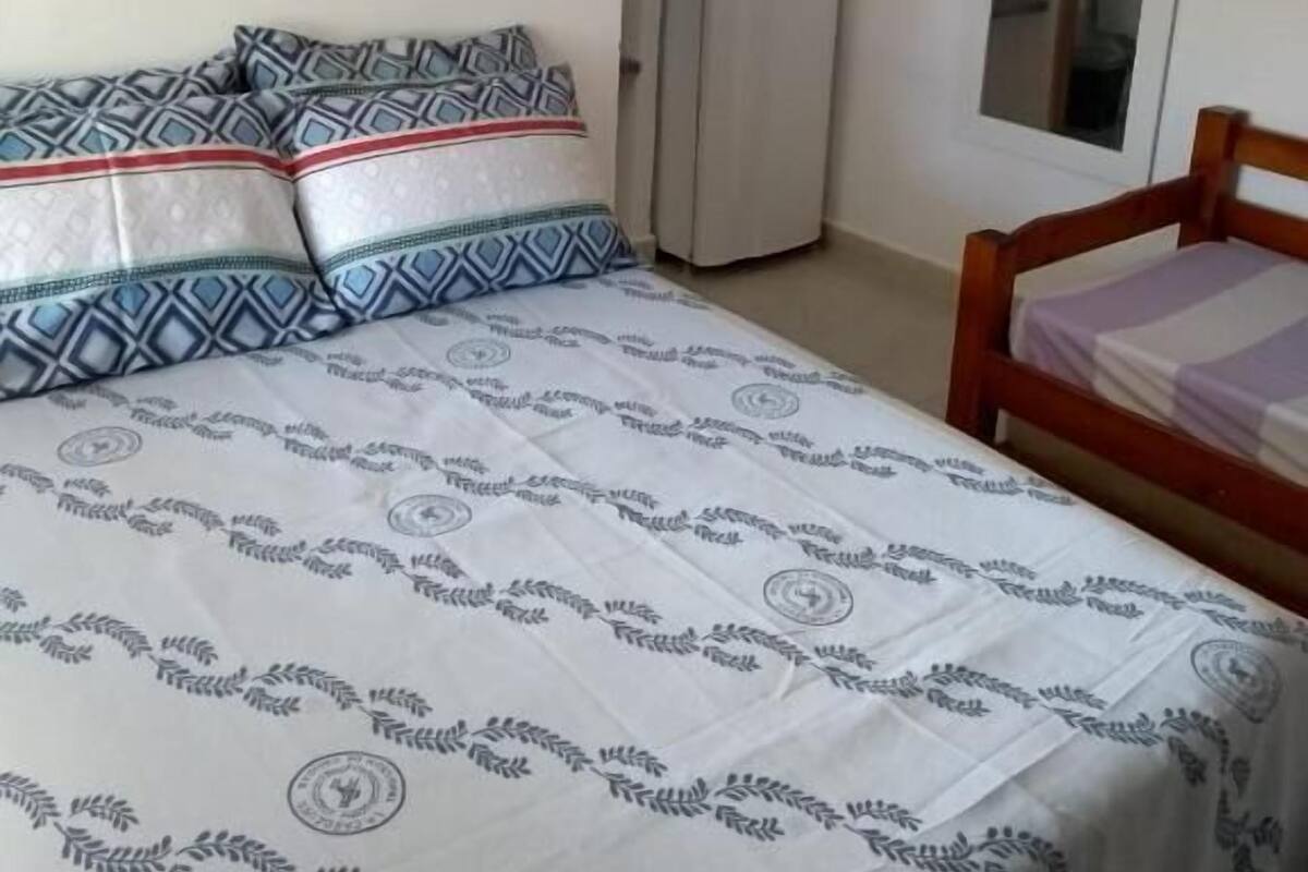 Un dormitorio con cama, almohadas, cabecera de madera, armario y un espejo en la pared.