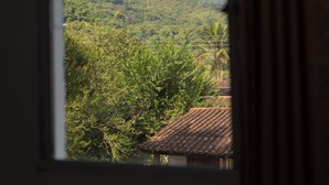 Blick aus dem Fenster auf eine üppige grüne Landschaft mit Palmen und einer entfernten Hügelkette.
