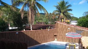 Ein Swimmingpool mit Holzzaun, einem Reetdach und einem gestreiften Sonnenschirm.