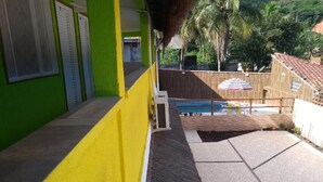 Ein Gebäude mit grüner und gelber Fassade, ein Poolbereich mit gefliestem Deck und im Hintergrund eine Sicht auf Palmen und ein Gebäude mit rotem Dach.