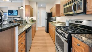 A modern kitchen with wooden cabinets, a stainless steel stove, a microwave, and a granite countertop. - Historic Biltmore Village Retreat | 2 King En-Suites | Fireplace | Pets Welcome (Asheville)