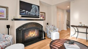 A living room with a fireplace, a television mounted above it, and a floral armchair. - Historic Biltmore Village Retreat | 2 King En-Suites | Fireplace | Pets Welcome (Asheville)