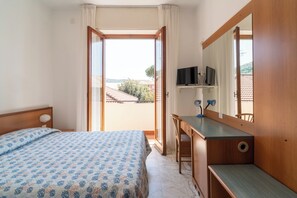 Un dormitorio con cama, escritorio, espejo y vistas al exterior.