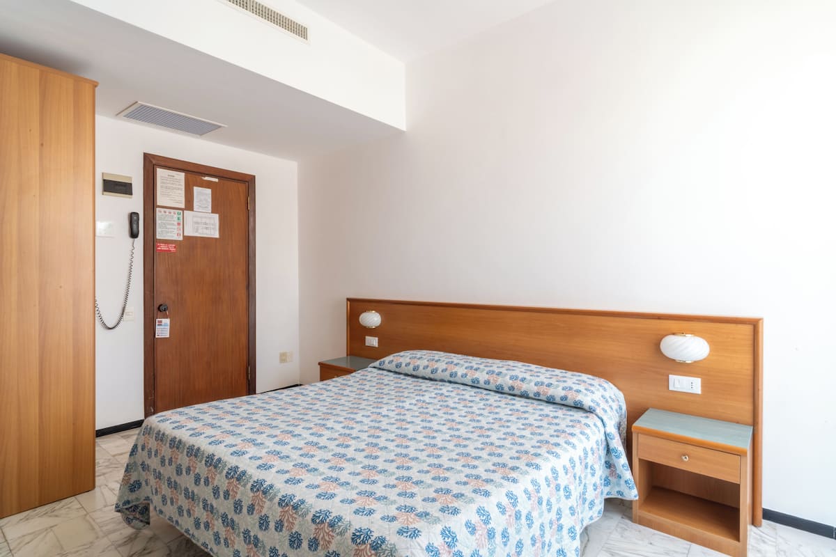 Un dormitorio con cama, armario de madera, mesita de noche y teléfono en la pared.