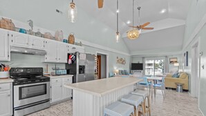 Cozinha moderna com armários brancos, uma ilha grande e um espaço de refeições com banquetas.