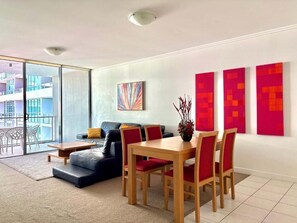 A modern living room with a sofa, dining table, chairs, and artwork on the wall.