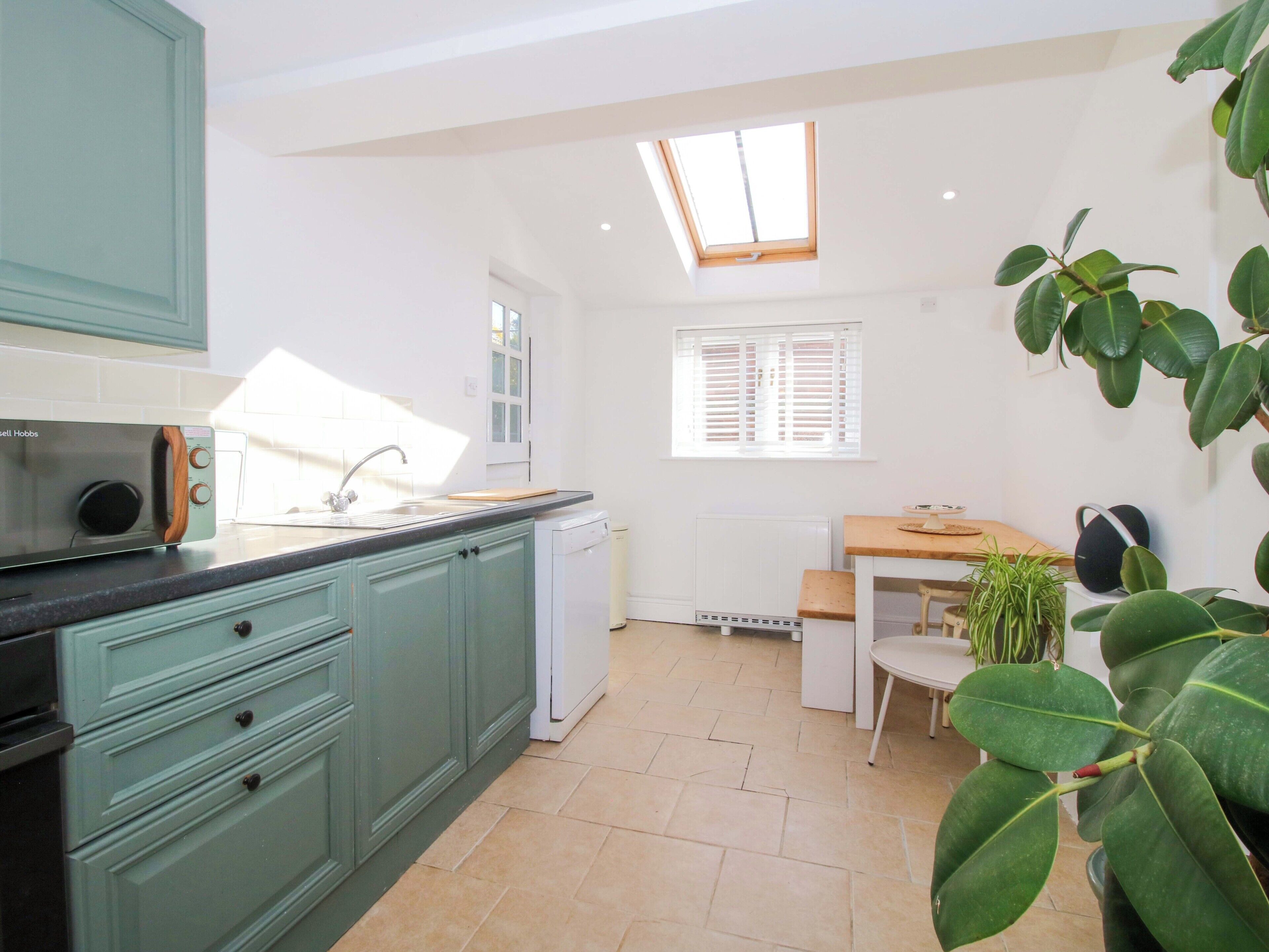 A kitchen with teal cabinets, a built-in microwave, a sink, a window with blinds, a radiator, and a dining area with a table and chairs.