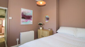 A bedroom with a bed, a radiator, a bedside table with a plant, a wall-mounted mirror, and a ceiling light fixture. - Cheshire Views (Malpas)