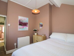 A bedroom with a bed, a radiator, a bedside table with a plant, a wall-mounted mirror, and a ceiling light fixture. - Cheshire Views (Malpas)
