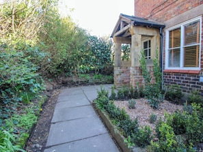 A garden pathway leading to a brick house with a window and a small covered area. - Cheshire Views (Malpas)