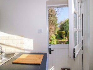 A kitchen with a wooden cutting board, a sink, and a window with a view of greenery. - Cheshire Views (Malpas)