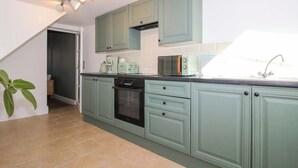 A kitchen with teal cabinets, a black oven, a microwave, and a coffee maker. - Cheshire Views (Malpas)
