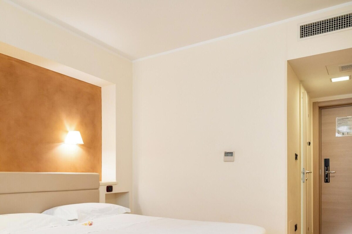 Ein Hotelzimmer mit einem Bett, zwei Wandleuchten und einer Tür zu einem anderen Raum.