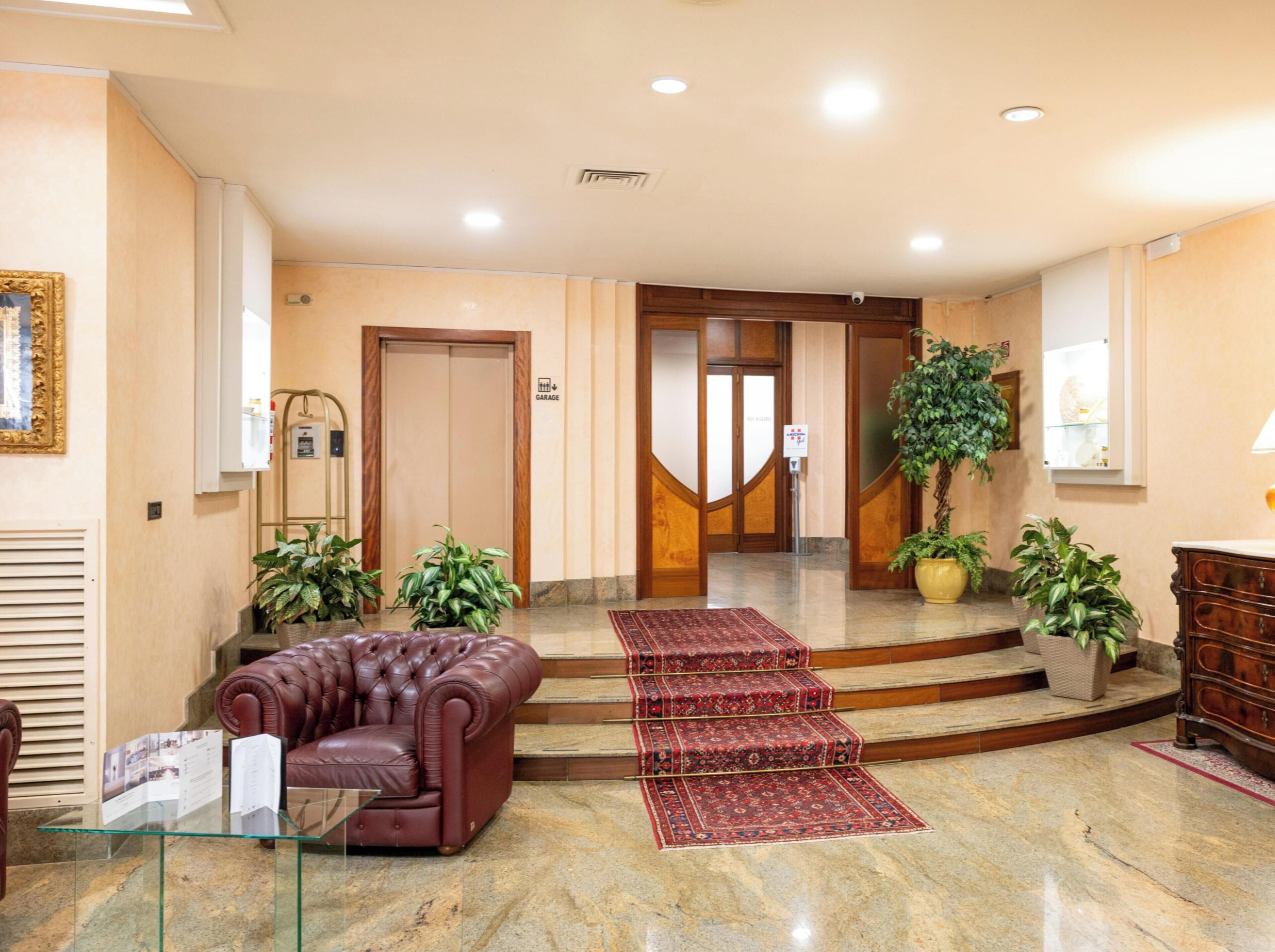 Un hall d’entrée avec un canapé en cuir, une table en verre, un escalier recouvert d’une moquette rouge et des plantes en pot.