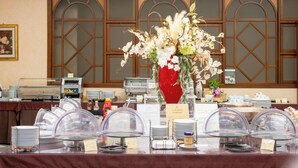 Un buffet disposé sous des cloches en verre transparentes, un vase rouge contenant des fleurs blanches et un panneau indiquant : « SUR DEMANDE ».
