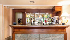 Un coin bar doté d’un comptoir en granit, d’étagères remplies de bouteilles, d’une machine à café et d’une lampe.