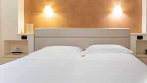 Une chambre d’hôtel avec un grand lit, deux tables de chevet et une tête de lit dotée de lampes fixées au mur.