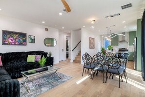 A modern living room with a black sofa, glass coffee table, and a dining area with metal chairs. - Austin’s Special, Arcade Game, PoolTable & Sleep16+ (Austin)