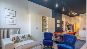 Ein modernes Wohnzimmer mit einer Couch, zwei blauen Sesseln, einem Esstisch und einer Küche im Hintergrund.