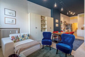 Ein modernes Wohnzimmer mit einer Couch, zwei blauen Sesseln, einem Esstisch und einer Küche im Hintergrund.