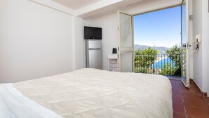 A bedroom with a bed, a television, a refrigerator, and a balcony with a view. - 'Fabian's House' with Sea View in Taormina (Taormina)