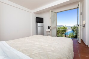 Una camera da letto con un letto, televisione, frigorifero e un balcone con vista.