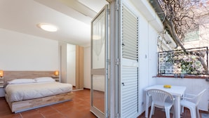 A bedroom with a bed, a sliding door, a small table with chairs, and a window with a view of trees. - 'Fabian's House' with Sea View in Taormina (Taormina)