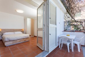 Una camera da letto con un letto, una porta scorrevole, un tavolino con sedie e una finestra vista alberi.