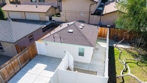 Patio trasero residencial con área cercada, un cobertizo pequeño y una casa con techo de tejas.
