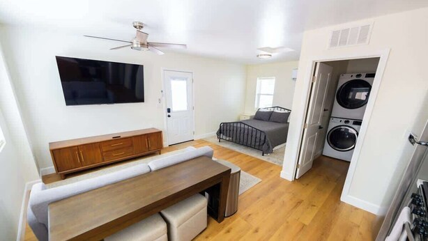 Una sala de estar moderna con una televisión de pantalla plana, muebles de madera, un ventilador de techo y un área de lavandería.