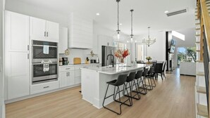 Une cuisine moderne avec des meubles blancs, des appareils en acier inoxydable et un îlot central doté de tabourets de bar.