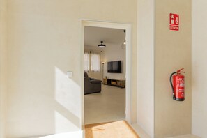 Ein Flur, der in einen Wohnbereich mit Sofa, Fernseher und einem an der Wand befestigten Feuerlöscher führt.