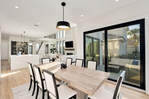 Uma cozinha moderna com uma ilha central, uma área de refeições com mesa e cadeiras de madeira, e um amplo vão de vidro deslizante que dá para um pátio externo.