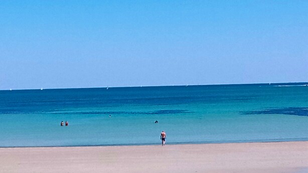 A beach with clear water and a person walking on the sand.